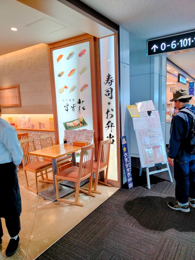 新千歳空港 保安検査後 搭乗待合室 「北の味覚すず花ゲート店」お寿司の看板 メニューを見る男性