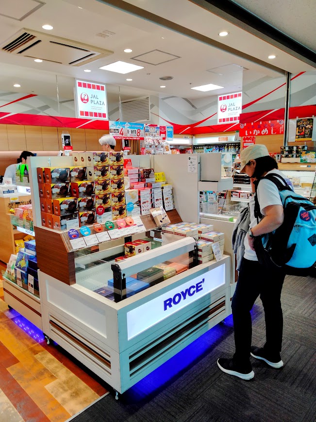 新千歳空港保安検査後エリア JALプラザ店内、ロイズチョコレートの前に立ち商品を選ぶ女性
